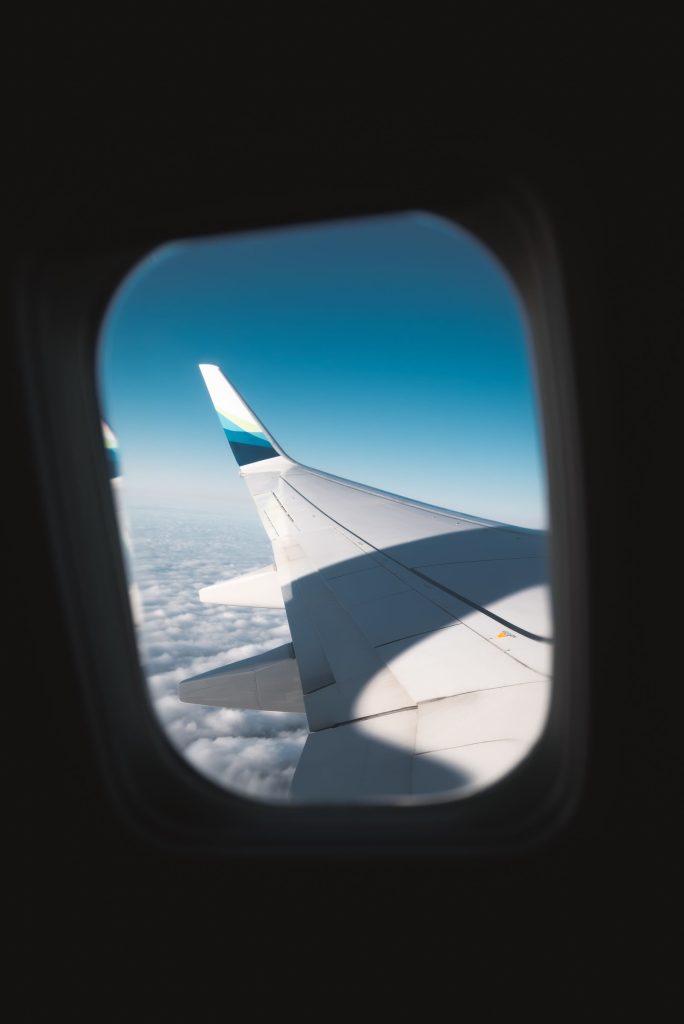 View of an airplane wing above the clouds through a cabin window